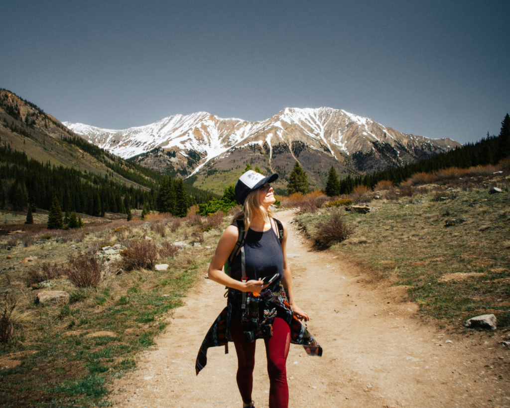 Woman hiking on a mountain trail with snow capped colorado peaks in the background.