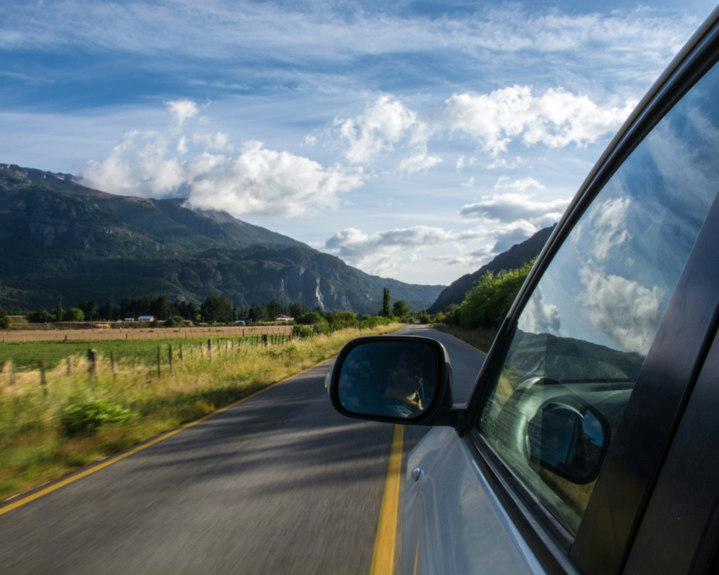View from a car window while driving through a mountain valley with clouds reflected in the glass.