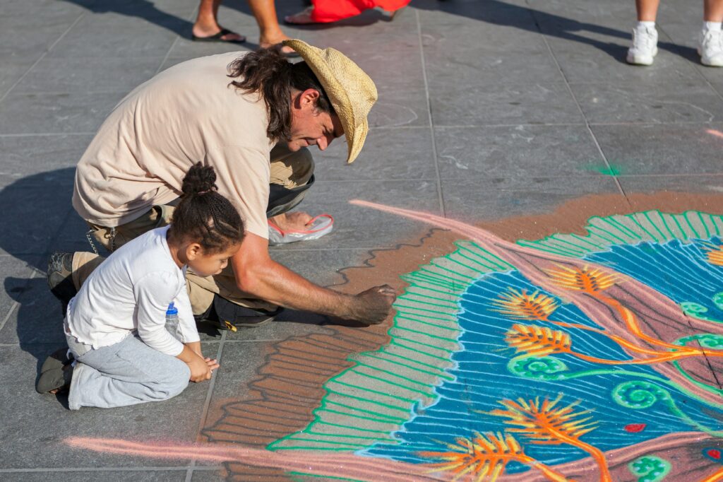 Artist creating colorful chalk art on a sidewalk while a child watches during an outdoor summer denver chalk art festival. Things to do in denver colorado in summer