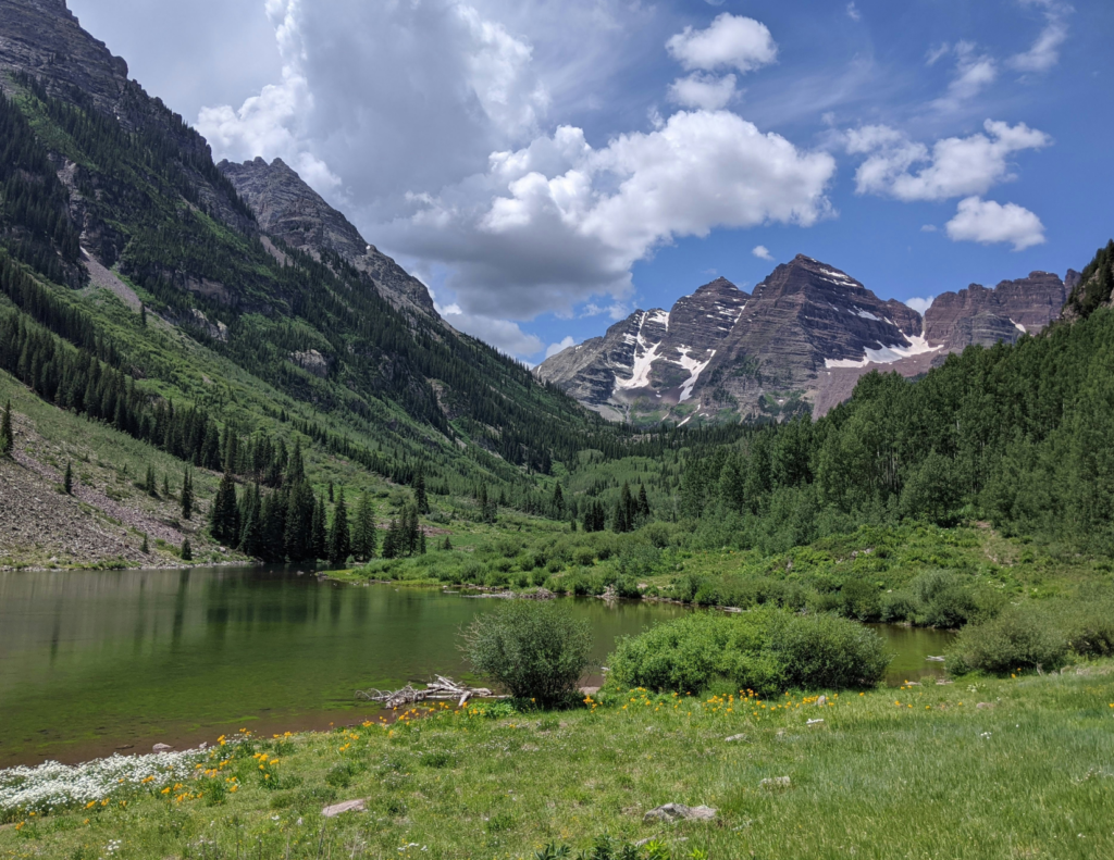 Best Colorado Towns For A Relaxing Colorado Weekend Trip 2 Scenic colorado mountain lake surrounded by green trees, wildflowers, and rugged peaks.