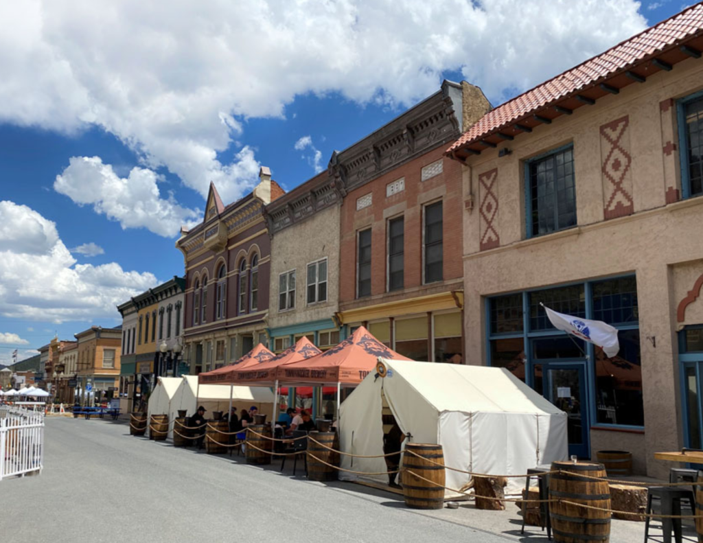 Best Colorado Towns For A Relaxing Colorado Weekend Trip 3 Historic colorado downtown street with colorful buildings, patio seating, and summer clouds.