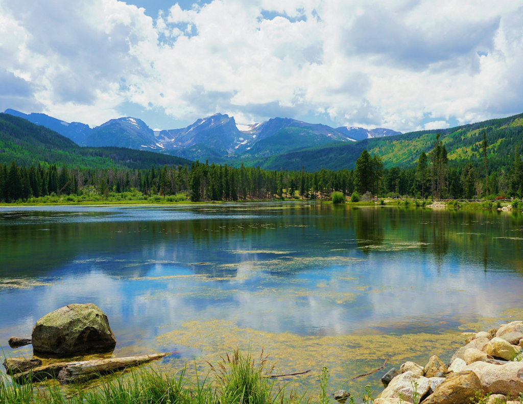 Best Colorado Towns For A Relaxing Colorado Weekend Trip 4 Peaceful colorado lake with green forests, mountain peaks, and clouds reflected in the water.